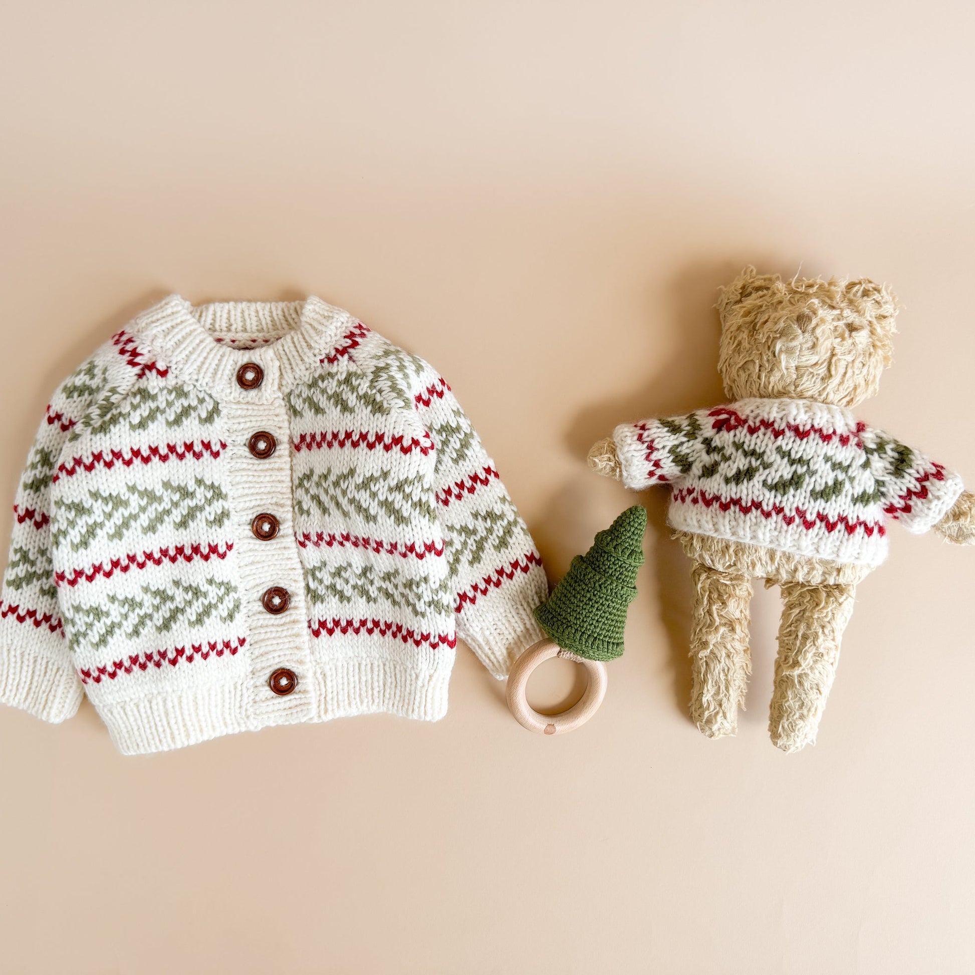 Knitted sweater with pattern and buttons, next to a toy wearing a similar sweater on a beige background