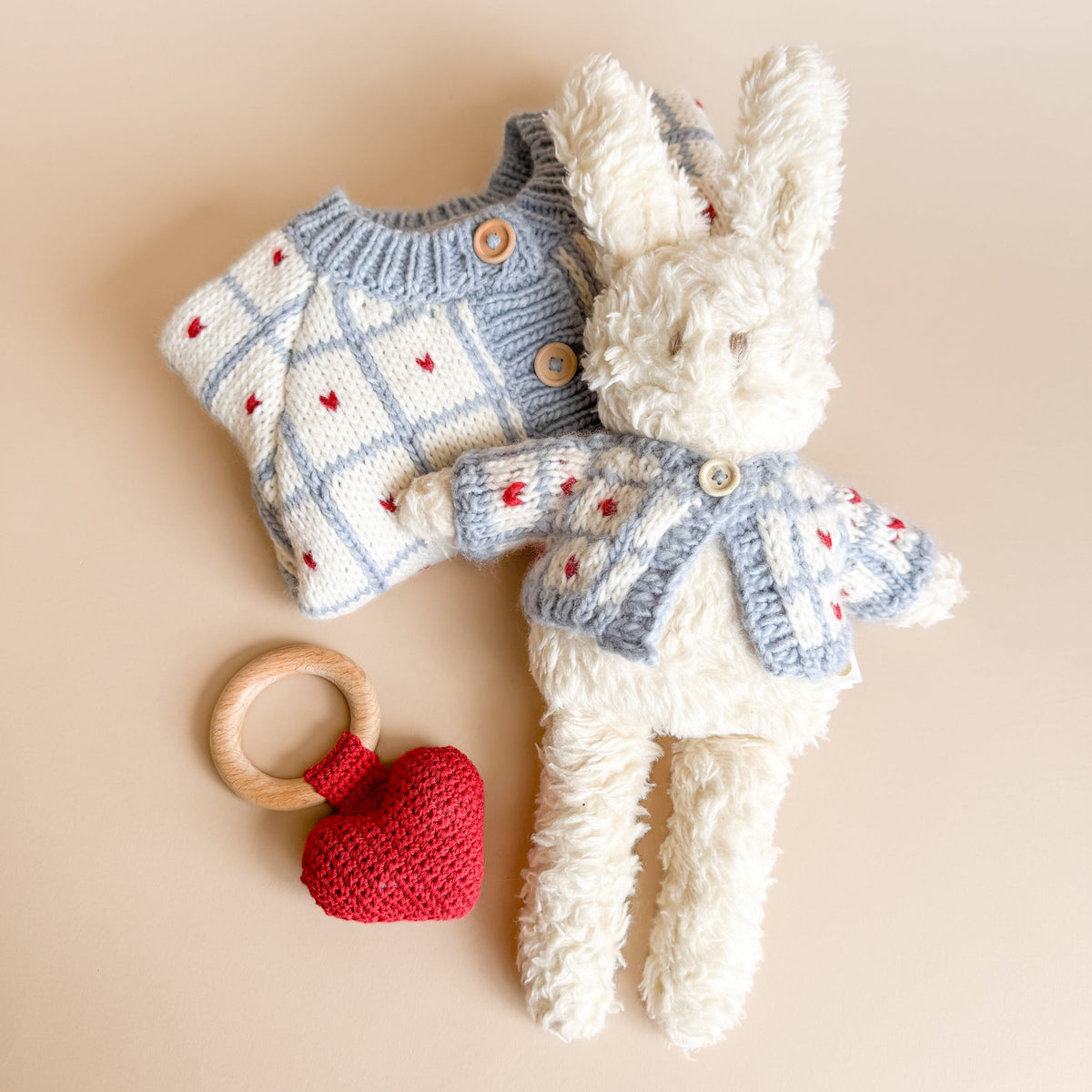 Knitted bunny toy with checkered jacket, wooden teething ring, and red heart on a beige background